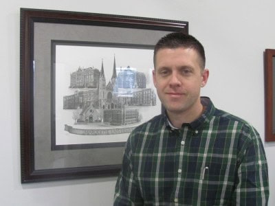 Man in plaid shirt smiling by framed architectural artwork