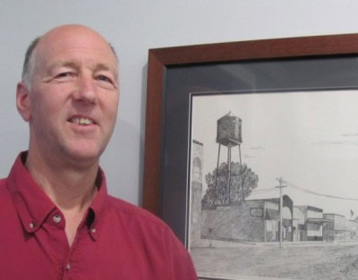 Man smiling beside framed drawing of water tower