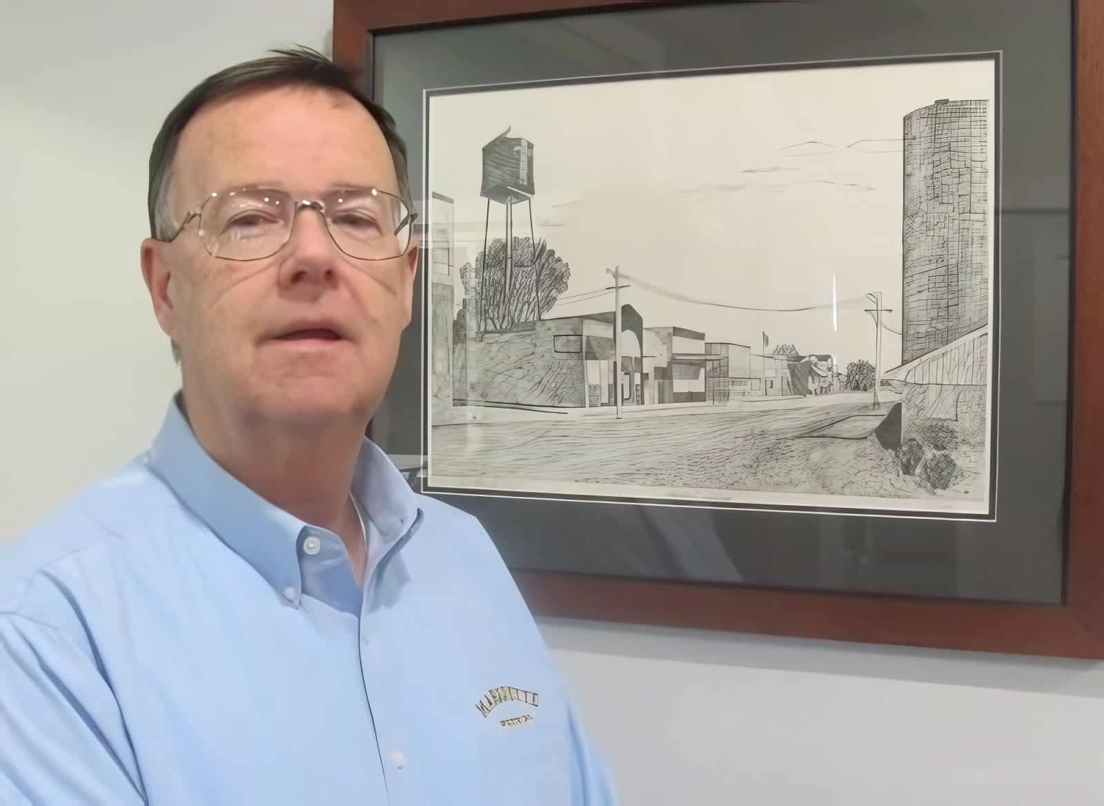 Man in blue shirt standing beside framed street sketch